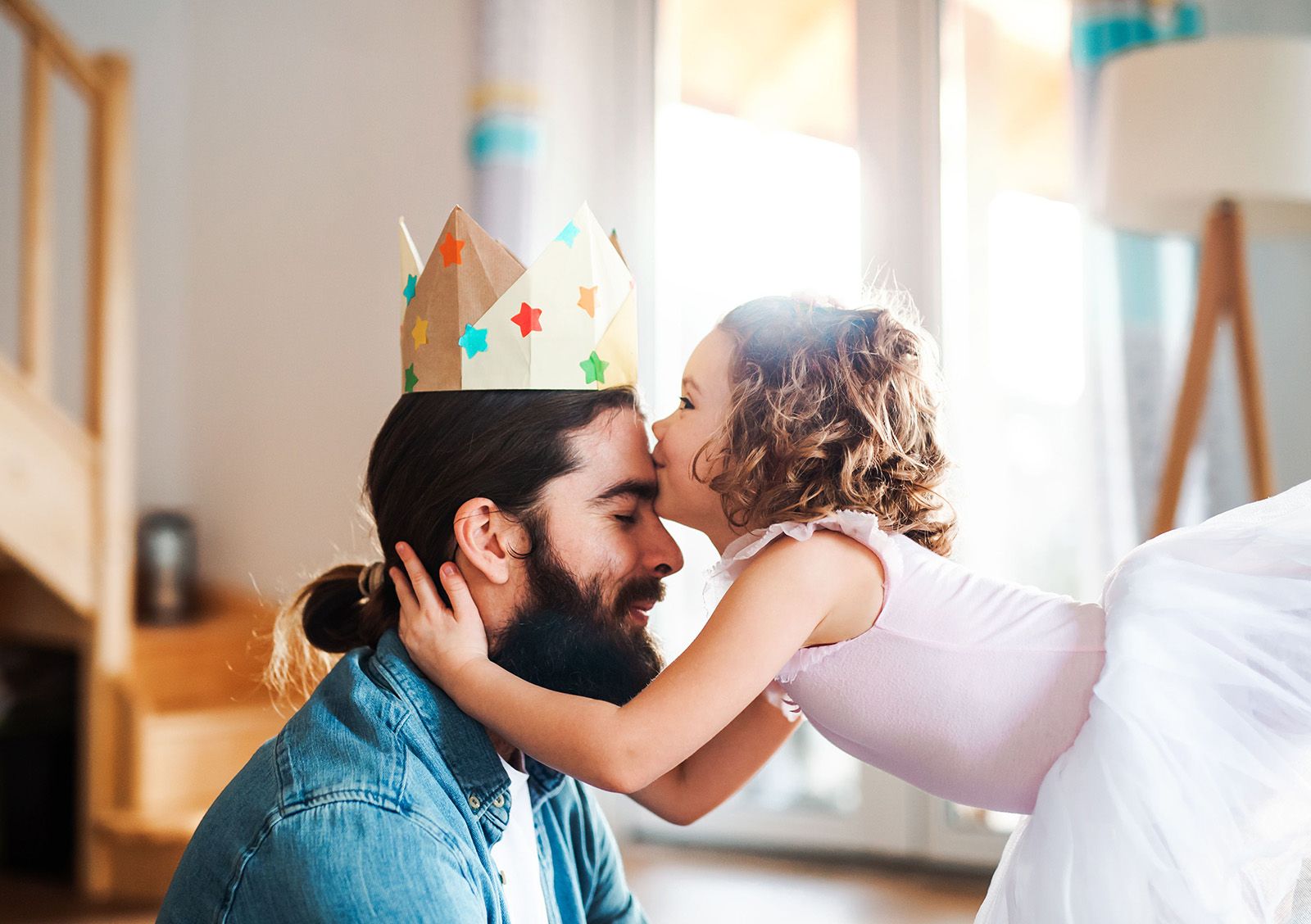 A side view of small girl with a princess crown and young father at home, playing.
