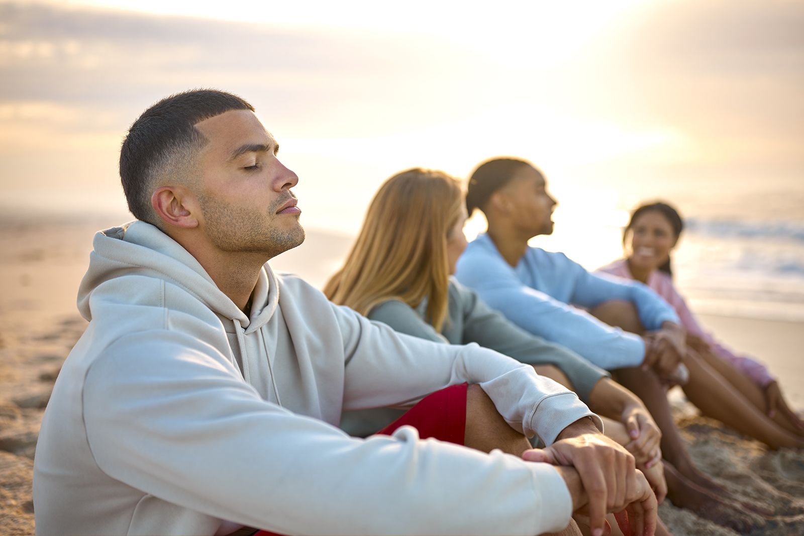 A man with closed eyes sitting on a bench, relaxing with his friends during a vacation.